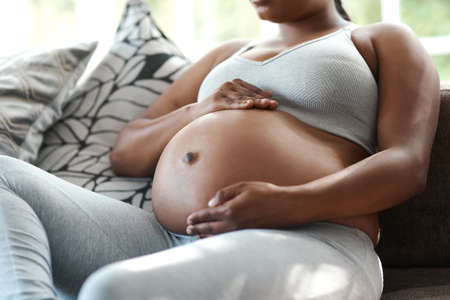 Sitting down to bond with her baby. Closeup shot of an unrecognisable woman touching her pregnant belly at home.の写真素材