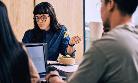 This salad is to tasty. a young businesswoman eating while with her coworkers.
