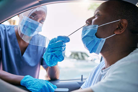 Doctor or nurse doing covid or corona virus test at a drive thru on a man sitting in a car. Medical professional taking nose swab sample from male patient through window with a PCR diagnostic kit.の写真素材