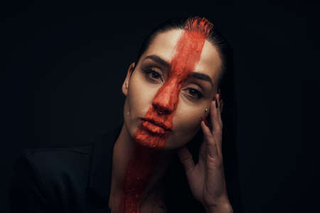 She has embraced the dark side. Studio shot of a young woman posing with paint on her face on a black background.の写真素材