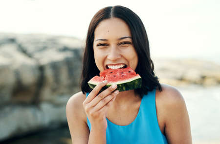 Fresh juicy watermelon is one of the best fruits. a young woman eating a slice of watermelon on the beach.の写真素材