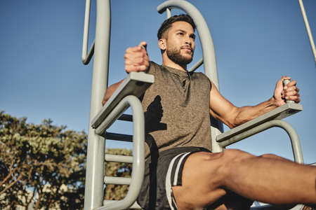 Spending some time out to build some muscle. Low angle shot of a muscular young man exercising at a...