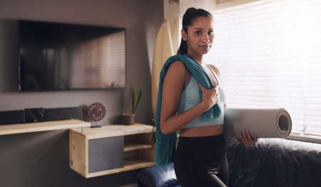 No excuses get that workout in. a young woman carrying her yoga mat after completing a workout routine at home.の写真素材