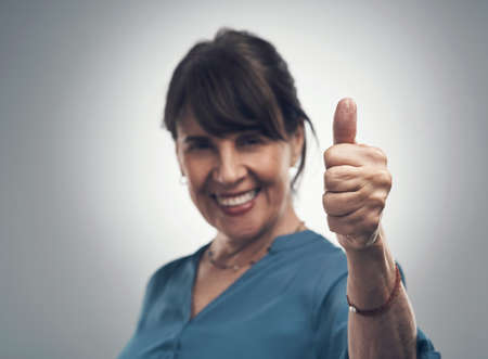 Well done on your sterling work. Studio portrait of a senior woman showing thumbs up against a grey background.の写真素材