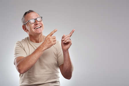 Check this out. a handsome mature man standing alone against a grey background in the studio and pointing at a promotion.の写真素材