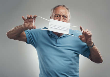 I think its meant to worn this way. an elderly man holding a protective face mask in a studio agains...