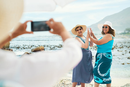 Capturing the moment and the memory. two mature friends standing and posing for a picture during a day out on the beach.の写真素材