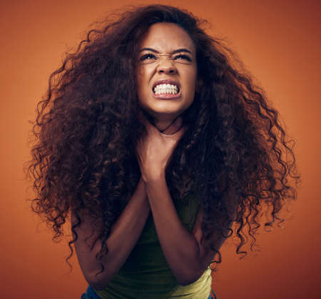 What do you want from me. a woman choking herself while standing against an orange background.の写真素材