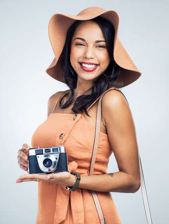 The one thing you need when traveling is your camera. Studio shot of a beautiful young woman holding a camera while standing against a white background.の写真素材