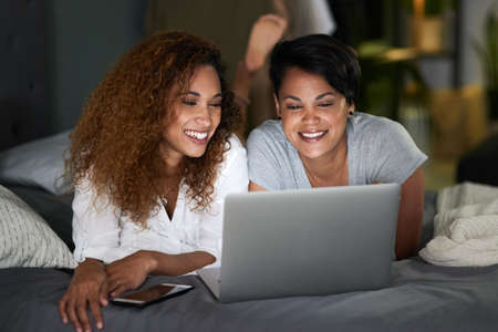 Do you think we should subscribe. a young couple using a laptop while lying on their bed.の写真素材