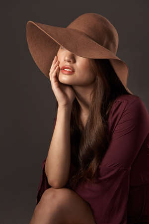 And the hat completes the look. an attractive young woman posing in studio against a grey background.の写真素材