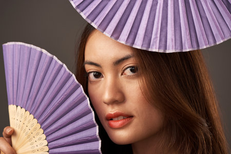 Whats a beauty without her adoring fans. Cropped portrait of an attractive young woman posing with fans in studio against a grey background.の写真素材