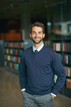 I work best in libraries. Cropped portrait of a handsome young businessman standing with his hands in his pockets in an empty library.の写真素材
