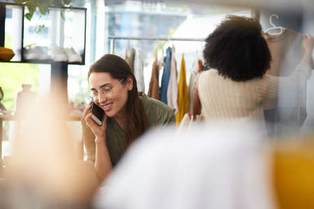 Youre welcome to pop in any time. a woman talking on her cellphone while working in a clothing...