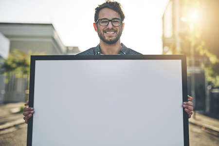 Copyspace, marketing and advertising with a young business man holding a blank sign or poster. Portrait of a creative male showing ad copy space to promote a startup, service or design companyの写真素材