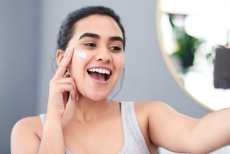 Rule number one of good makeup application is great skincare. beautiful young woman gleefully taking a photo of her face with a new moisturiser.の写真素材