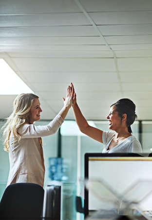 Teamwork, support and happy colleagues sharing high five in a modern office, excited about good news or feedback. Female coworkers celebrating success, expressing joy and collaborating on projectの写真素材