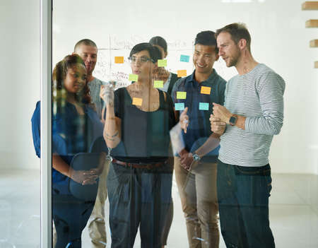 Group meeting for brainstorming ideas, creative projects or designs using sticky notes on glass...