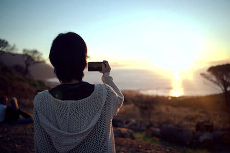 I like posting pictures of nature on my feed. a woman taking pictures on her cellphone of the...