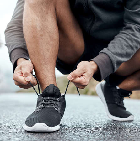 Prepare for your greatest run ever. Closeup shot of an unrecognisable man tying his shoelaces while...