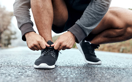 Good running shoes goes a long way. Closeup shot of an unrecognisable man tying his shoelaces while exercising outdoors.の写真素材