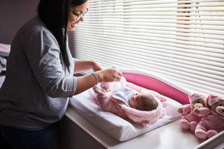 Nothing makes a baby feel more secure than routine. a young woman changing her baby girls clothing at home.の写真素材