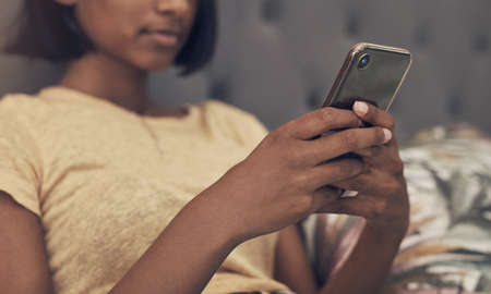 We dont have to feel alone just became were staying home. a woman using a smartphone while relaxing on her bed at home.の写真素材