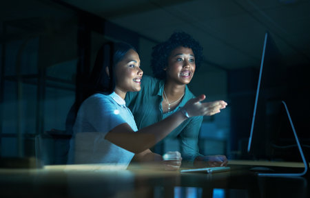 Good communication gets good results. two young businesswomen using a computer together during a late night at work.の写真素材