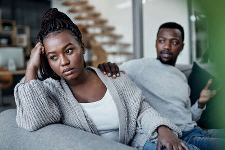 Closing the gap starts with reaching out. a young couple reaching out to his wife after having an argument on the sofa at home.の写真素材