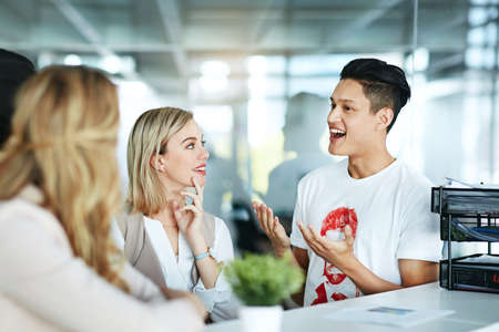 Happy and smiling design team talking while having a casual chat in a modern office. Diverse group of designers discussing an idea, planning a creative strategy for innovation at the workplaceの写真素材