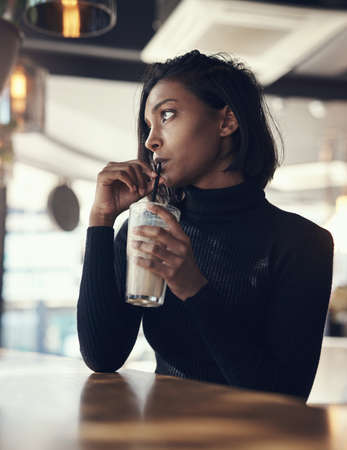 Iced coffee is for every season. a beautiful young woman drinking a iced coffee in a cafe.