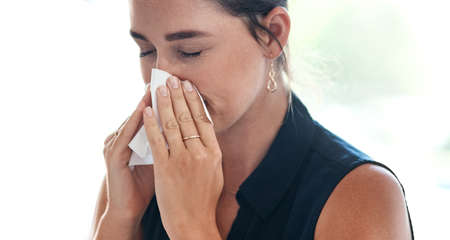 Her allergies are flaring up again. a young businesswoman blowing her nose in an office.