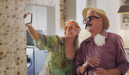 Say cheese. a happy senior couple standing together in costume and using a cellphone to take...