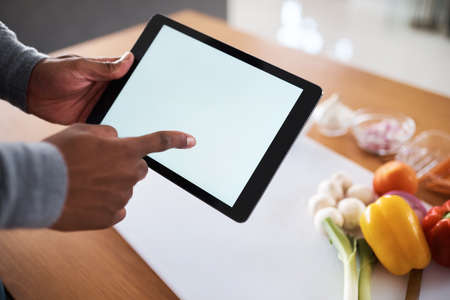 You can cook like a pro if you have the right resources. an unrecognizable man using a digital tablet while cooking at home.の写真素材