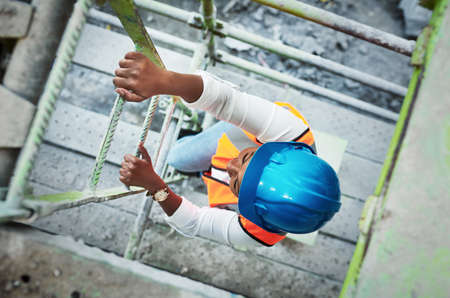 The harder you work the higher you go. a young woman climbing up a ladder at a construction site.