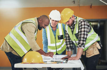 The right plan is a firm foundation for success. a group of builders going over building plans at a...