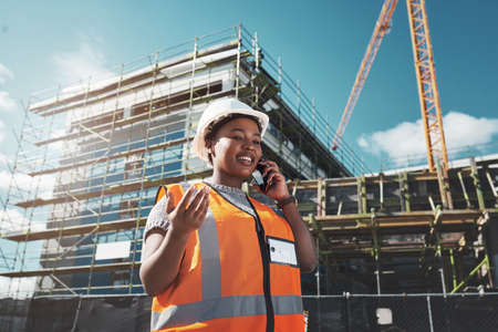 With her clients every step of the way. a young woman using a smartphone while working at a construction site.の写真素材