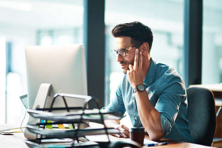 Professional corporate business man working on computer, browsing the internet and completing a project while sitting at a desk alone at work. One manager checking and reading emails online in officeの写真素材