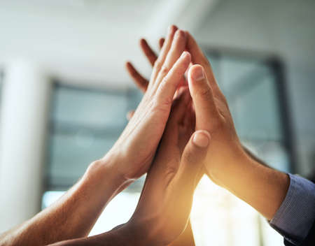 High five of a diverse group of businesspeople celebrate, unite and support each other. Closeup of a multiethnic corporate professional team hands touching showing success inside a startup officeの写真素材