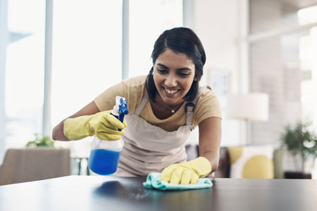 A clean home is a safe home. a young woman disinfecting a table at home.の写真素材