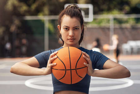 Gaining the skills to win takes time and patience. Portrait of a sporty young woman holding a basketball on a sports court.の写真素材