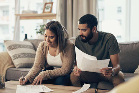 Taking the right steps to stay on financial track. a young couple going over paperwork at home.の写真素材