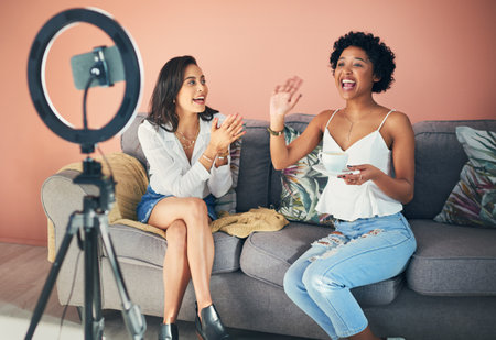 My friend is joining us today to spill the latest tea. two young women sitting together while recording a video for their blog at home.の写真素材