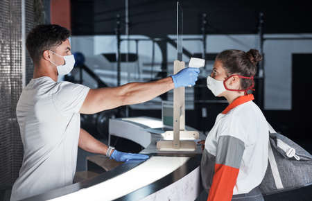 Putting screening processes in place to ensure everyones safety. a young woman getting her temperature taken with an infrared thermometer in a gym.の写真素材