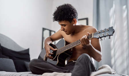 Good music makes your heart beat along with it. a young man playing the guitar in his bedroom at home.の写真素材