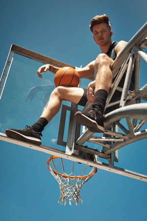 Reach for the sky or dont even try. Portrait of a sporty young man sitting on a basketball hoop on a...