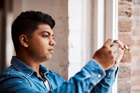 The view from up here is really great. a young businessman taking a picture from a window at work.