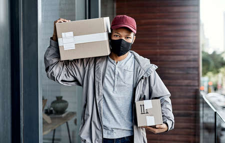 When it comes to safety and convenience, we always deliver. a masked young man delivering a package to a place of residence.の写真素材
