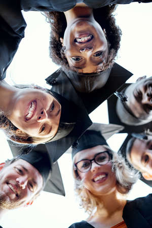 Their big smiles tell of their great success. Portrait of a group of students putting their heads together in a huddle on graduation day.の写真素材