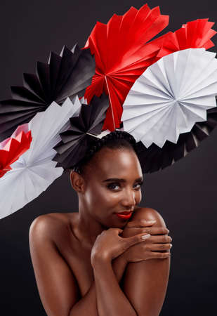 Bold colours that just accentuate her beauty. Studio shot of a beautiful young woman posing with a origami fans against a black background.の写真素材
